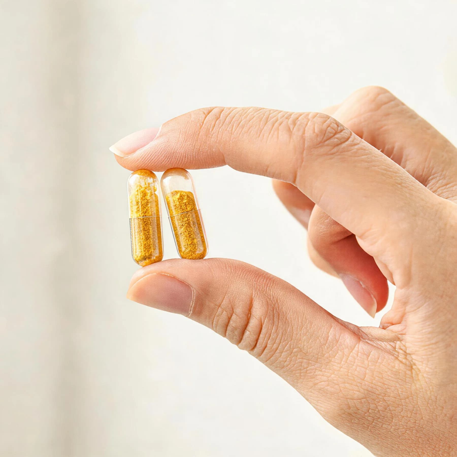 Two supplement capsules held between fingers